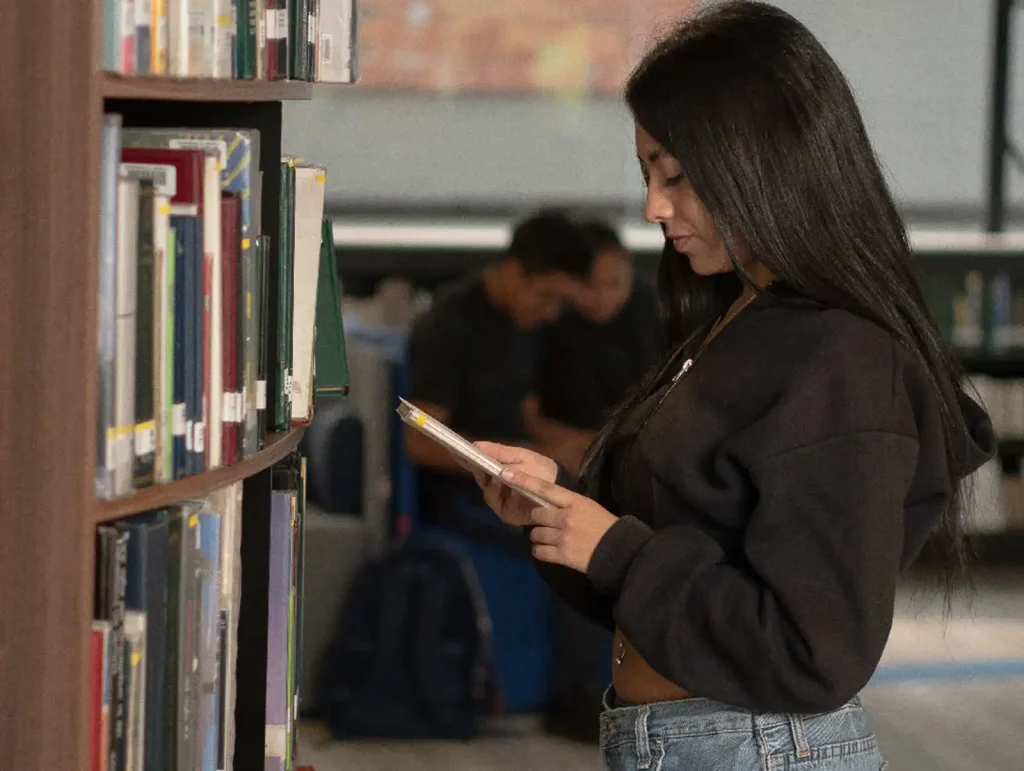Estudiante consultando libro en la biblioteca del CRAI Universidad de América.