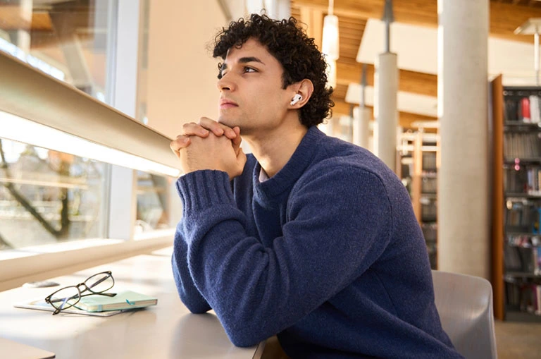 Estudiante universitario reflexionando en biblioteca antes de elegir su carrera profesional