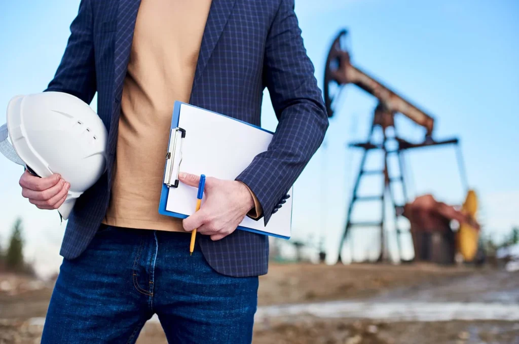 Gerencia de la industria petrolera con profesional sosteniendo casco y documentos en campo de extracción de petróleo