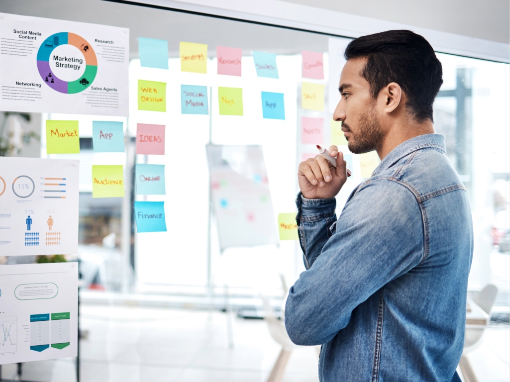 Profesional revisando una estrategia de trabajo frente a un panel con notas y gráficos para planificar programas de capacitación en la empresa.