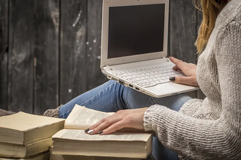 Estudiante leyendo un libro mientras utiliza un computador portátil, representando la importancia de la lectura, el pensamiento crítico y los tiempos de Inteligencia Artificial en la educación y el desarrollo de Colombia.